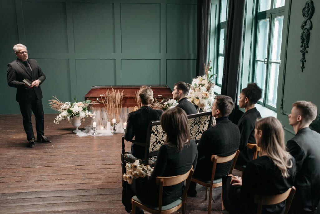 Group gathered indoors for a solemn funeral ceremony, expressing sorrow and remembrance.